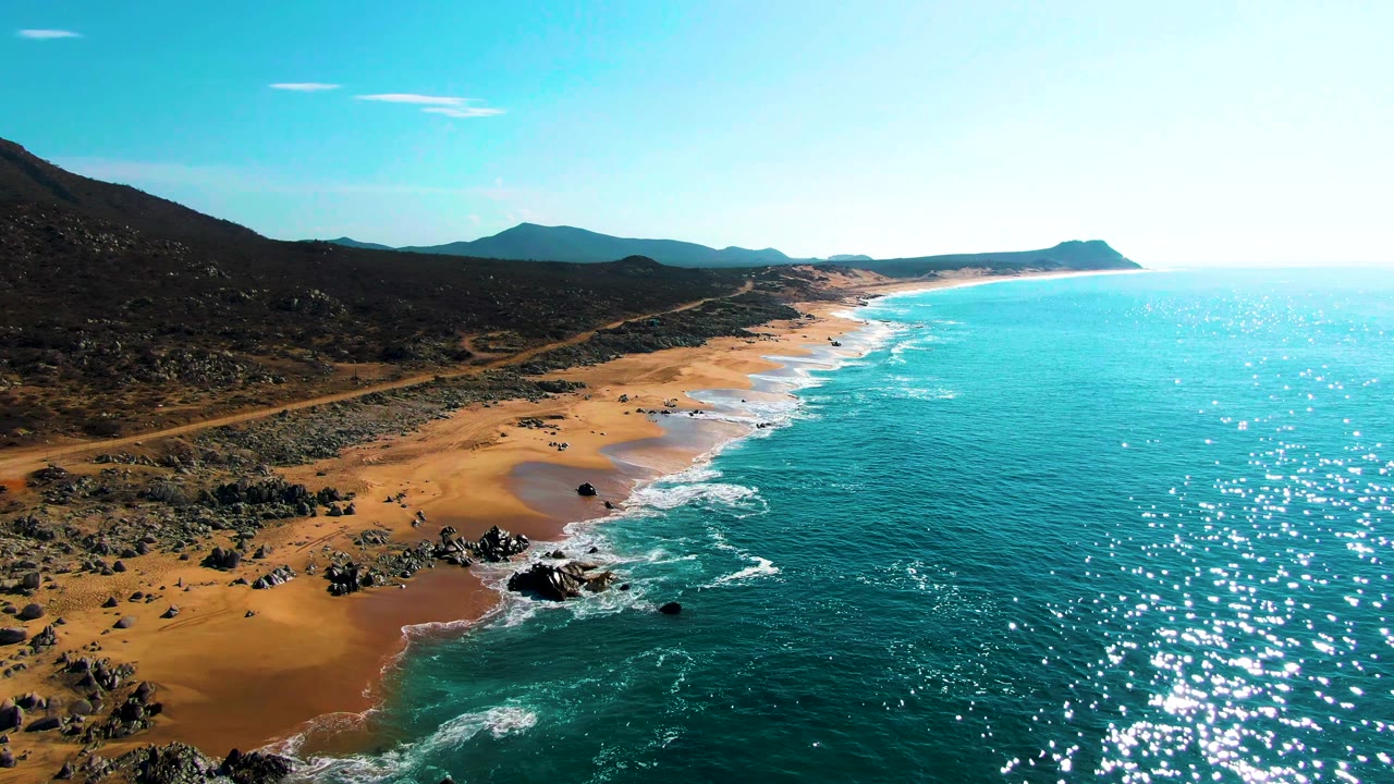 Aerial view of turquoise waves beside sandy beach and rocky shoreline