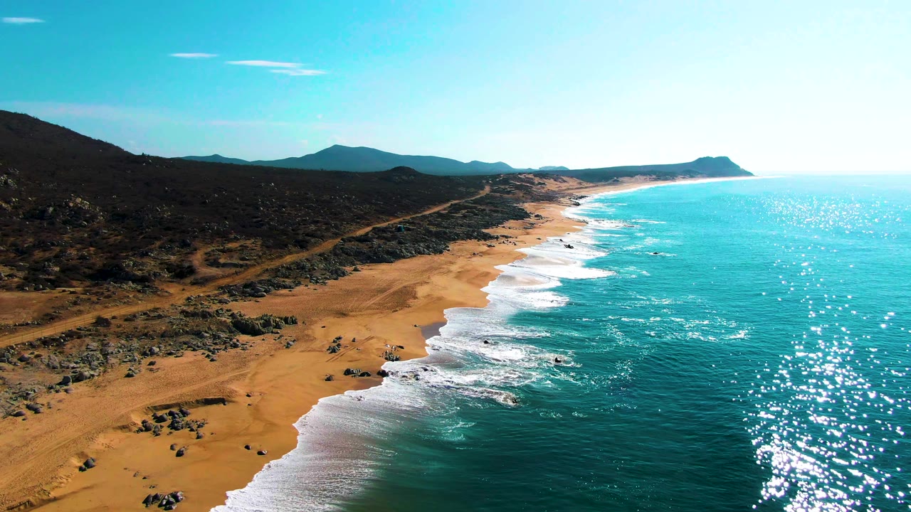 Aerial coastline view with surf wrapping around rocks near the sandy shore.