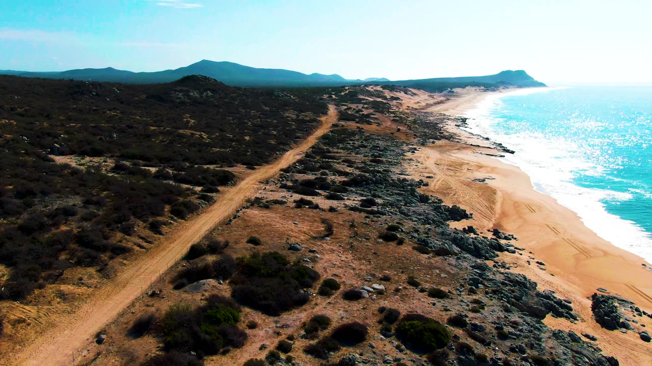 Aerial view of a coastal dirt road with sandy beach and waves.