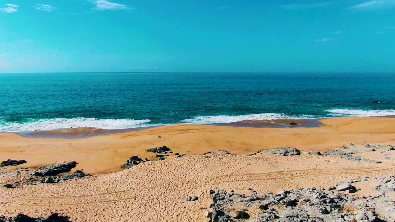 Rocky foreground above a sandy beach and blue ocean waves.