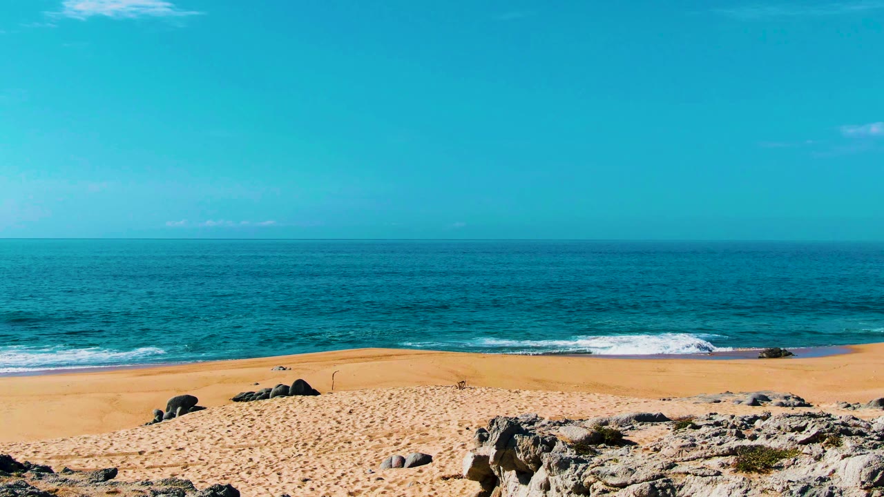 Wide beach, ocean horizon, rocks, sand, and blue sky
