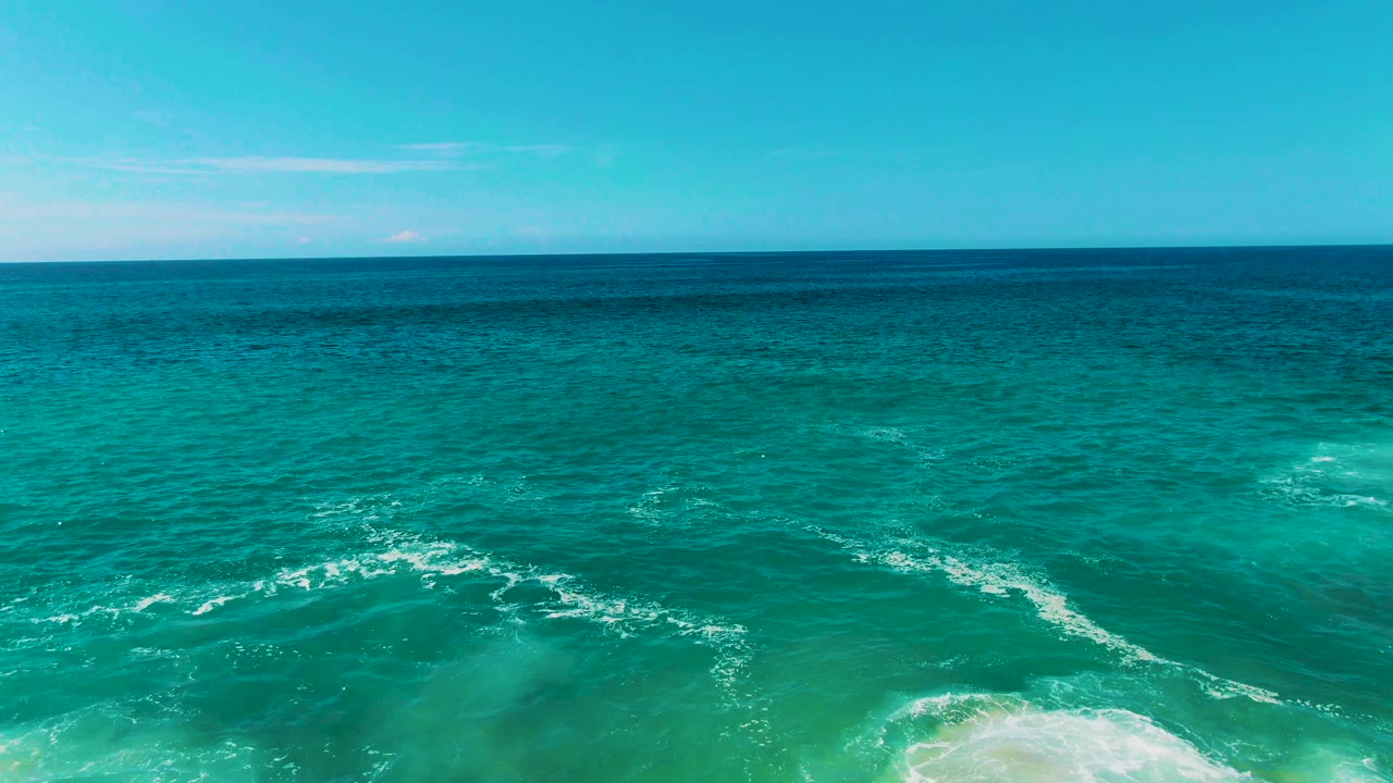 Wide turquoise sea with faint foam lines and distant horizon.