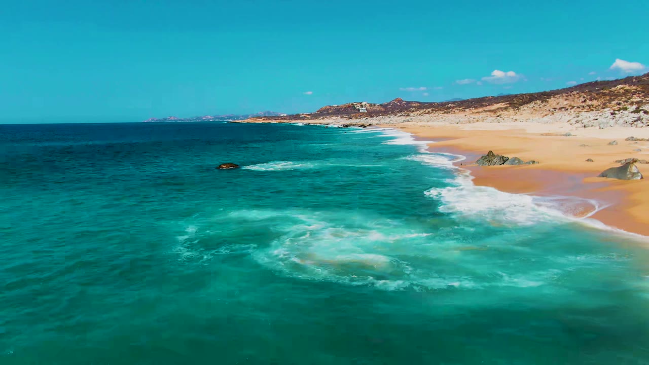 Turquoise ocean waves breaking beside a sandy beach and rocky shoreline.