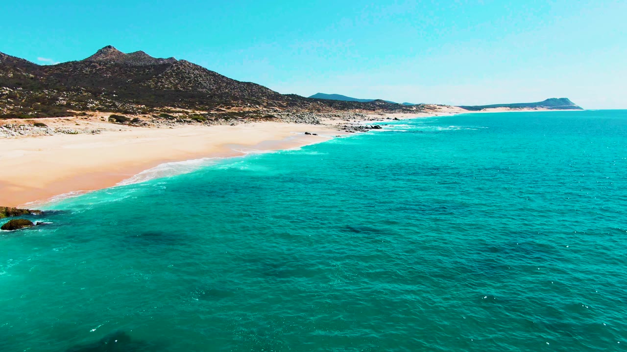 Beach and turquoise ocean with rocks near the lower left edge.