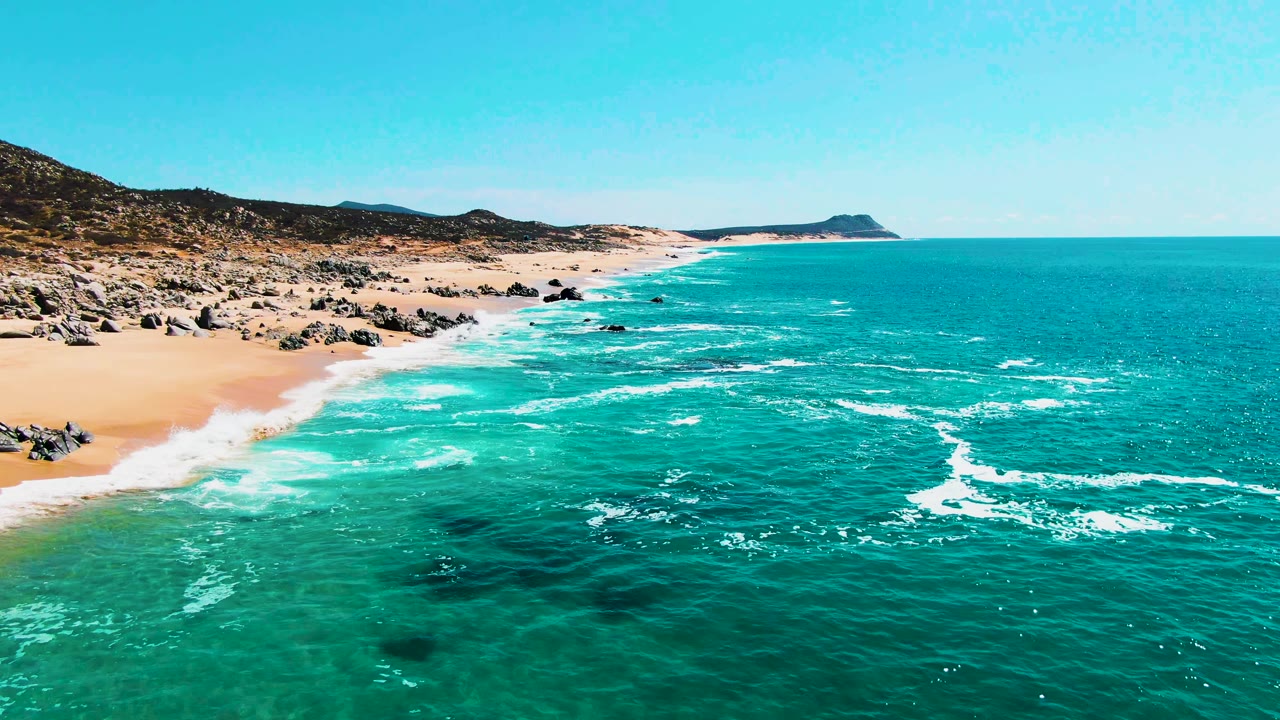 At two seconds, Buzzards Beach appears with more open ocean in the foreground, a broad band of whitewater near shore, rocky sand at left, distant landform, and no visible people.