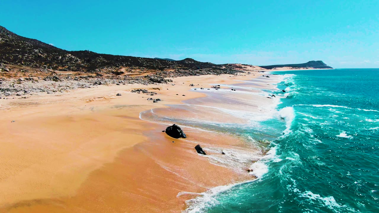 Drone view along beach with waves curling around exposed rocks