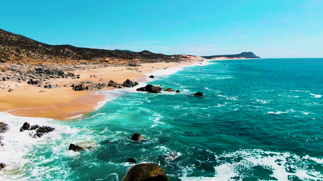 Sandy beach and rocky outcrops with foamy surf moving in from the lower left.