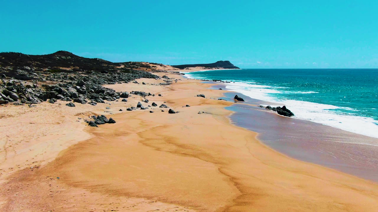 Rocky sand beach with waves breaking beside a turquoise ocean.
