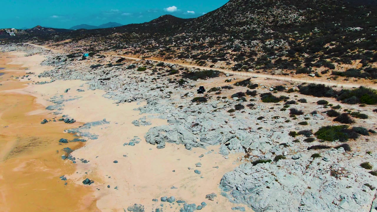 Aerial angle over a pale sand and rock field next to a dirt road.