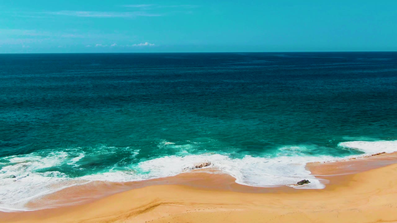 Wide aerial view of turquoise surf breaking onto a sandy beach