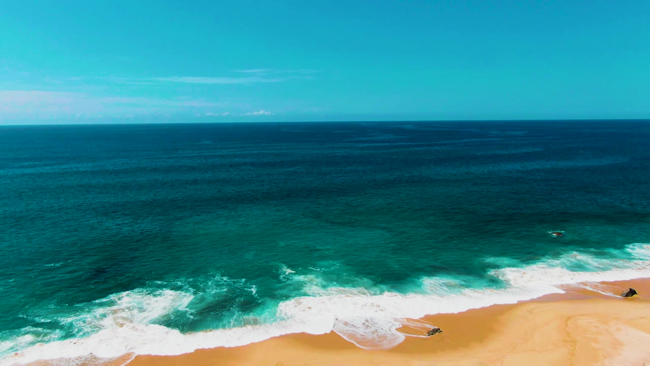At 0:01, Punta Buzzards surf pushes farther onto the sand, with a broad white foam band below dark blue water and no visible people.
