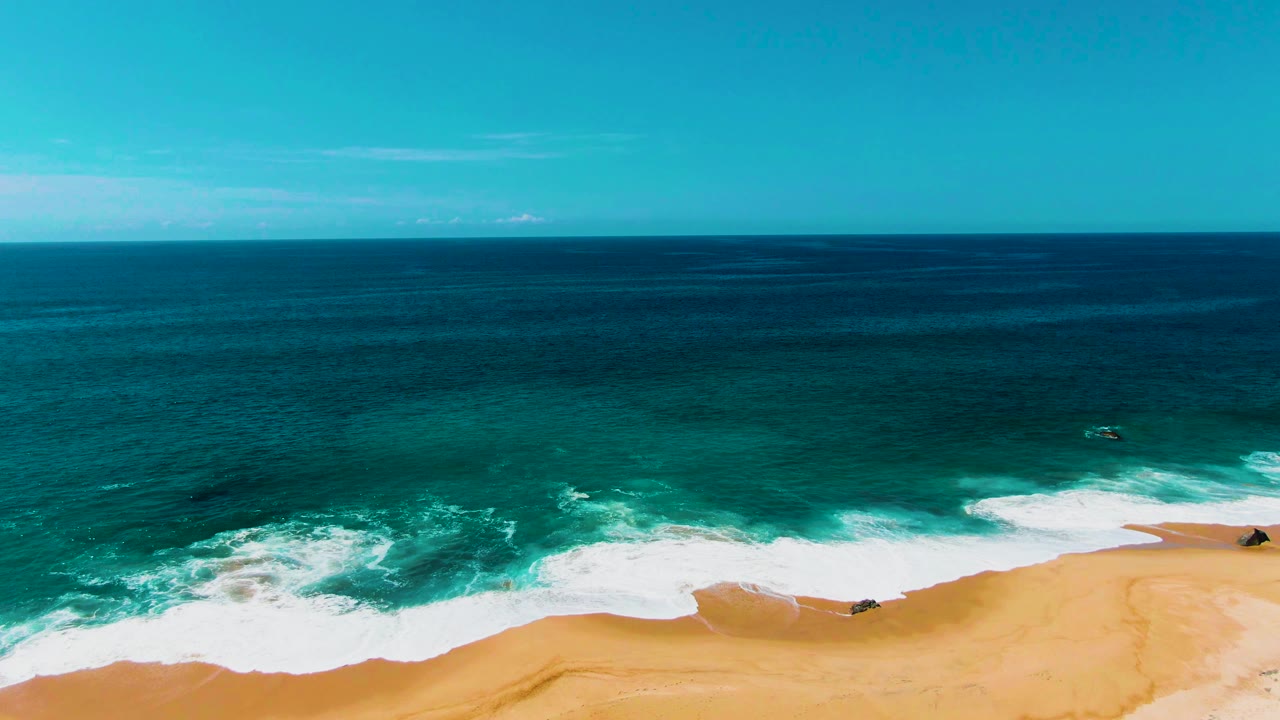 High aerial view of ocean swells breaking into foam along a sandy shore.
