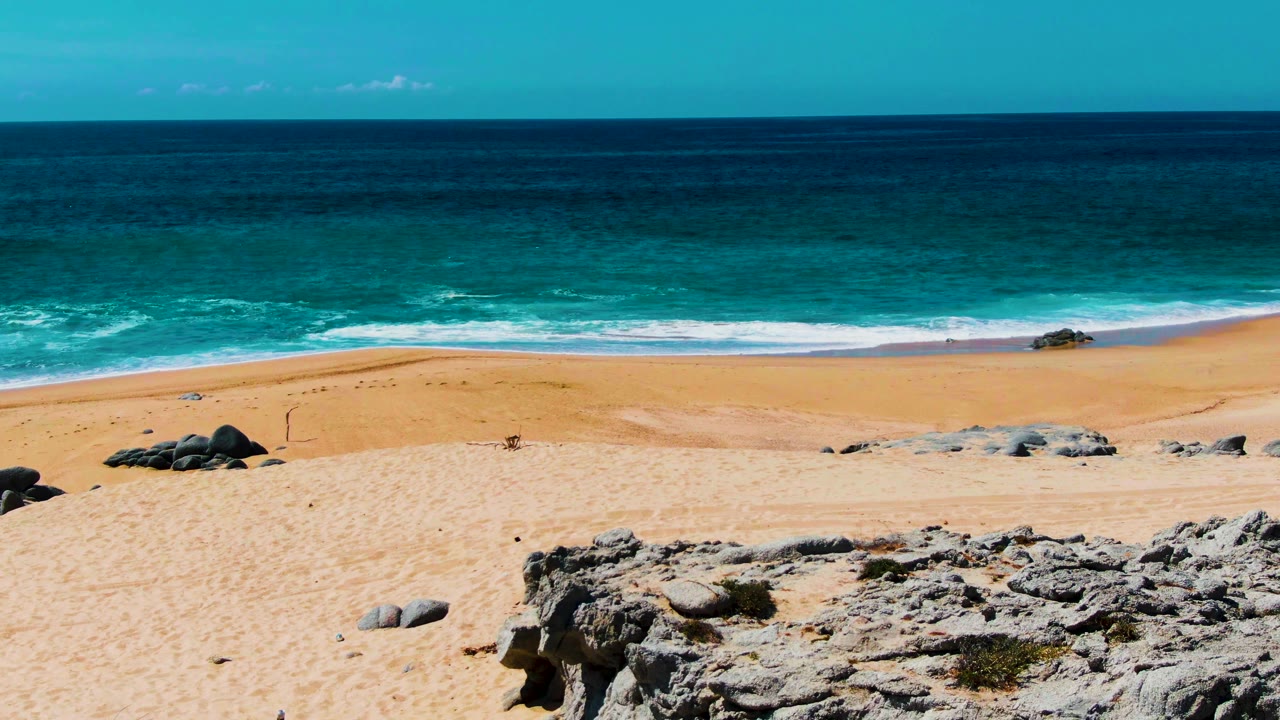 Open beach with ocean waves, pale sand, and rocks in the lower frame.