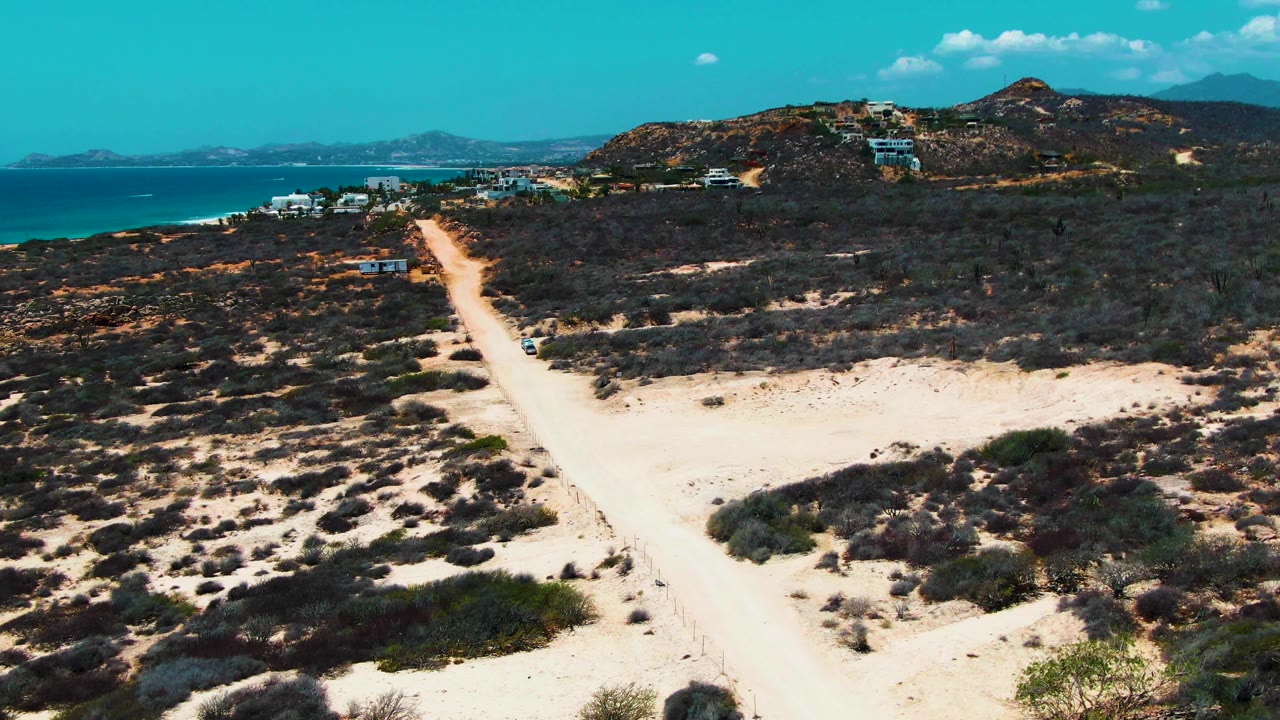A car appears on a pale dirt road through coastal desert brush.