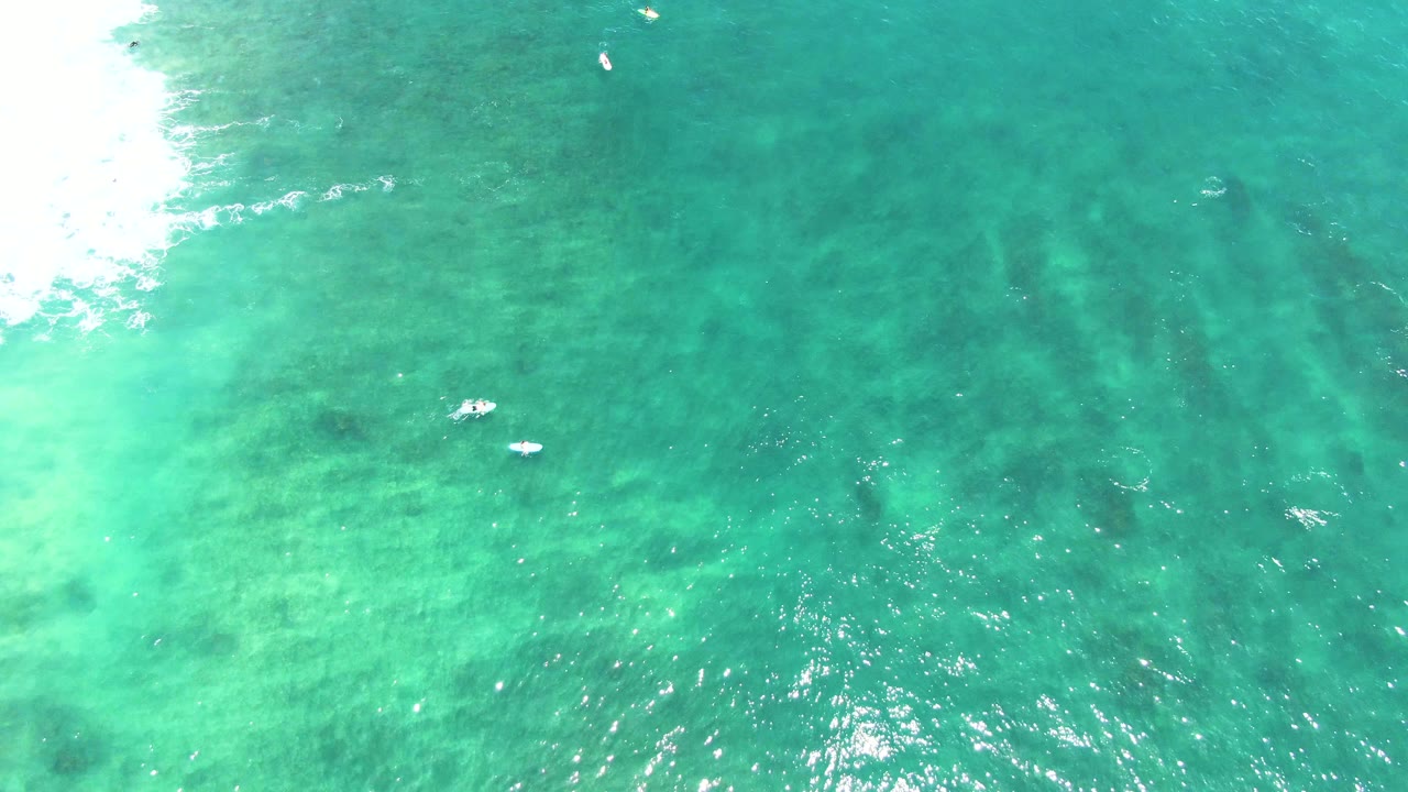 Clear green-blue ocean seen from above with small white floating shapes.