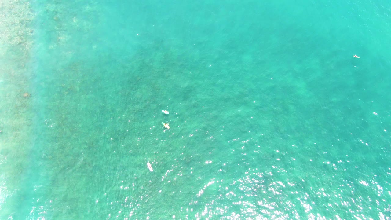 Overhead view of turquoise water at Punta Buzzards, Baja California Sur, with small swimmers near the left and lower portions of the frame and bright sun reflection on ripples.