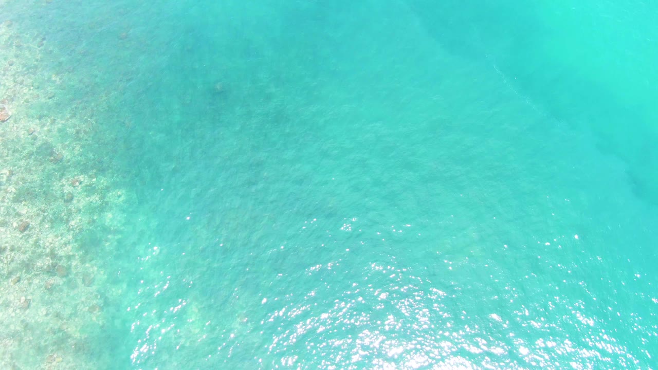 Opening frame of turquoise water over shallow coral and sand at Buzzards Beach in Baja California Sur, with sun glints near the lower center and no visible people.