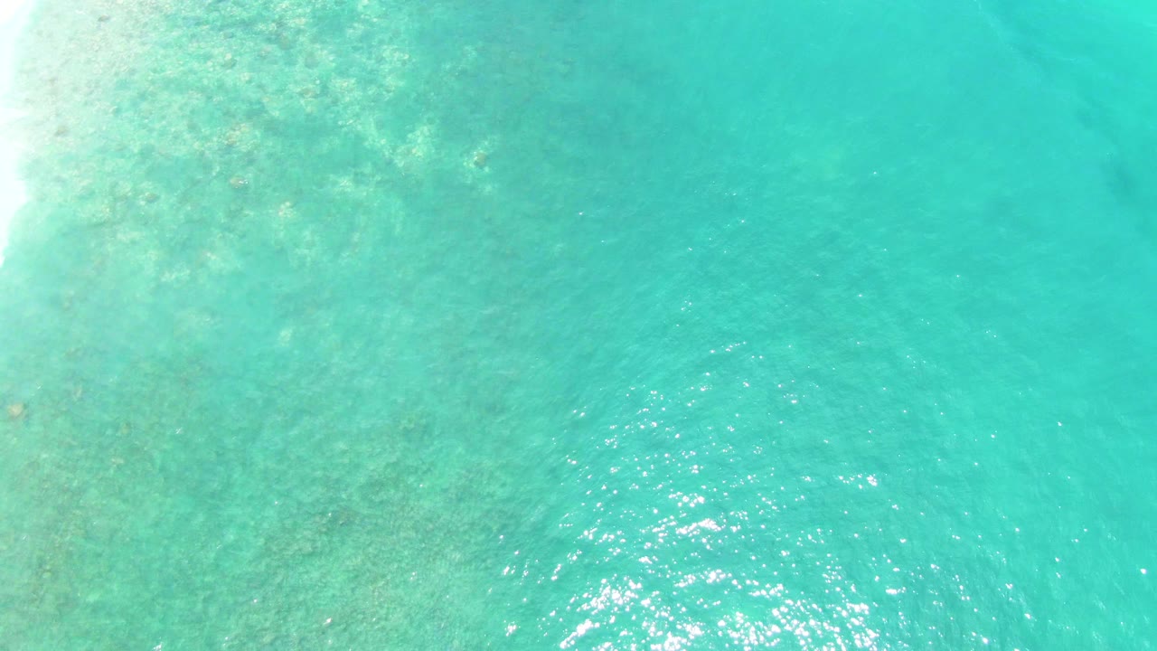 Clear shallow ocean with seabed patches and bright reflections