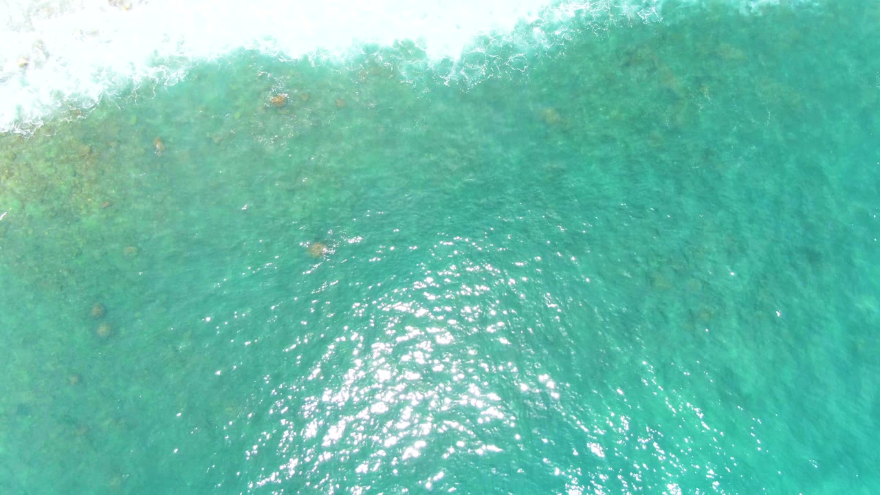 Overhead Punta Buzzards water view with the white foam band wider at the top, small darker patches below the surface, bright specular highlights, and no visible people.