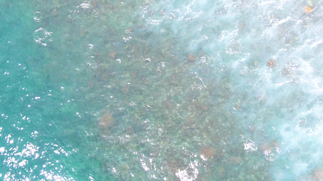 Overhead turquoise water with pale foam and rocky seabed below.