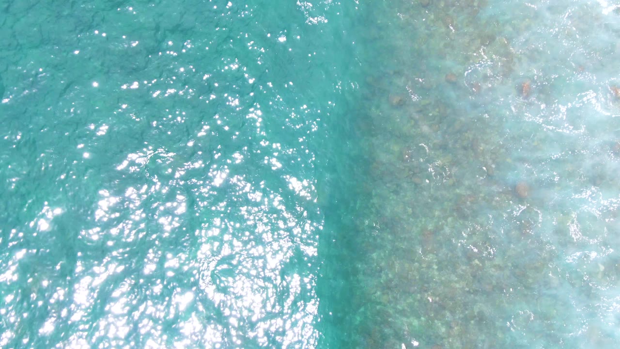 At Buzzards Beach in Baja California Sur, clear turquoise water reveals mottled underwater rocks beside a band of pale surface wash, with no visible people.