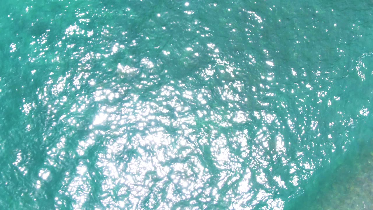 At Buzzards Beach in Baja California Sur, a straight-down view shows rippling turquoise water filled with dense white sun reflections and little seabed detail, with no visible people.