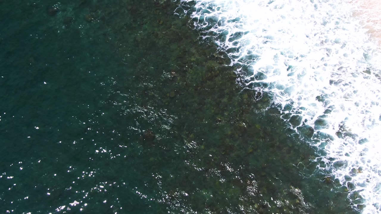 White foam breaks diagonally across deep green water at Buzzards Beach, with darker submerged texture visible beneath the surface and no visible people.