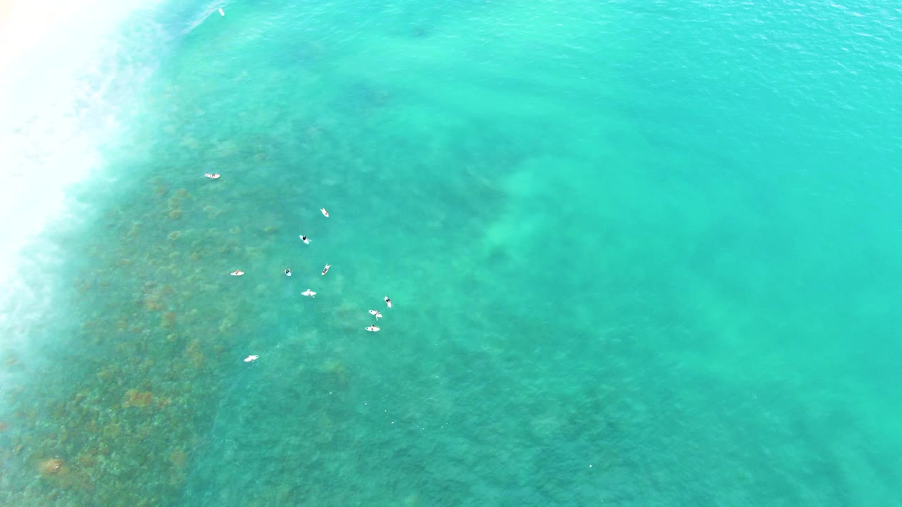 Swimmers scattered in clear turquoise shallows beside breaking surf.