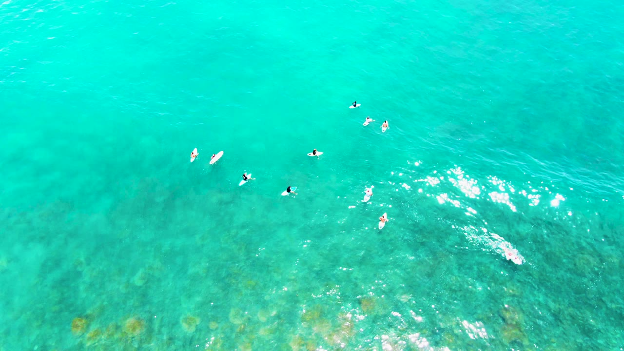 Aerial surfboard paddlers over clear blue-green water