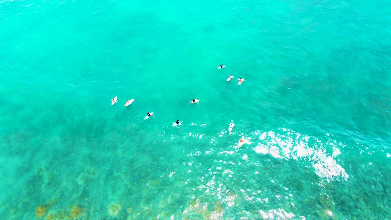 Top-down Punta Buzzards ocean view with surfboard paddlers dispersed near small white foam breaks and darker water patterns beneath the surface.