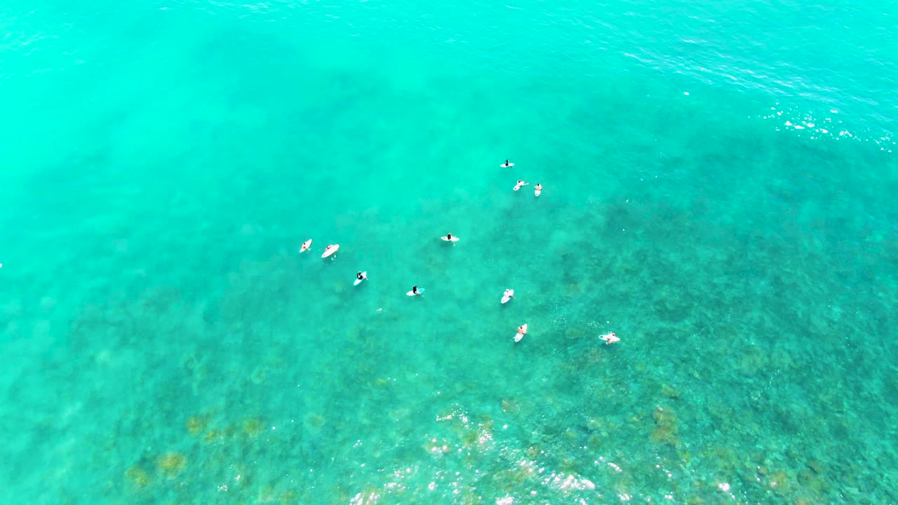 At two seconds, the aerial view holds on small people floating in clear Punta Buzzards water, with brighter reflections near the lower edge and darker underwater texture below.