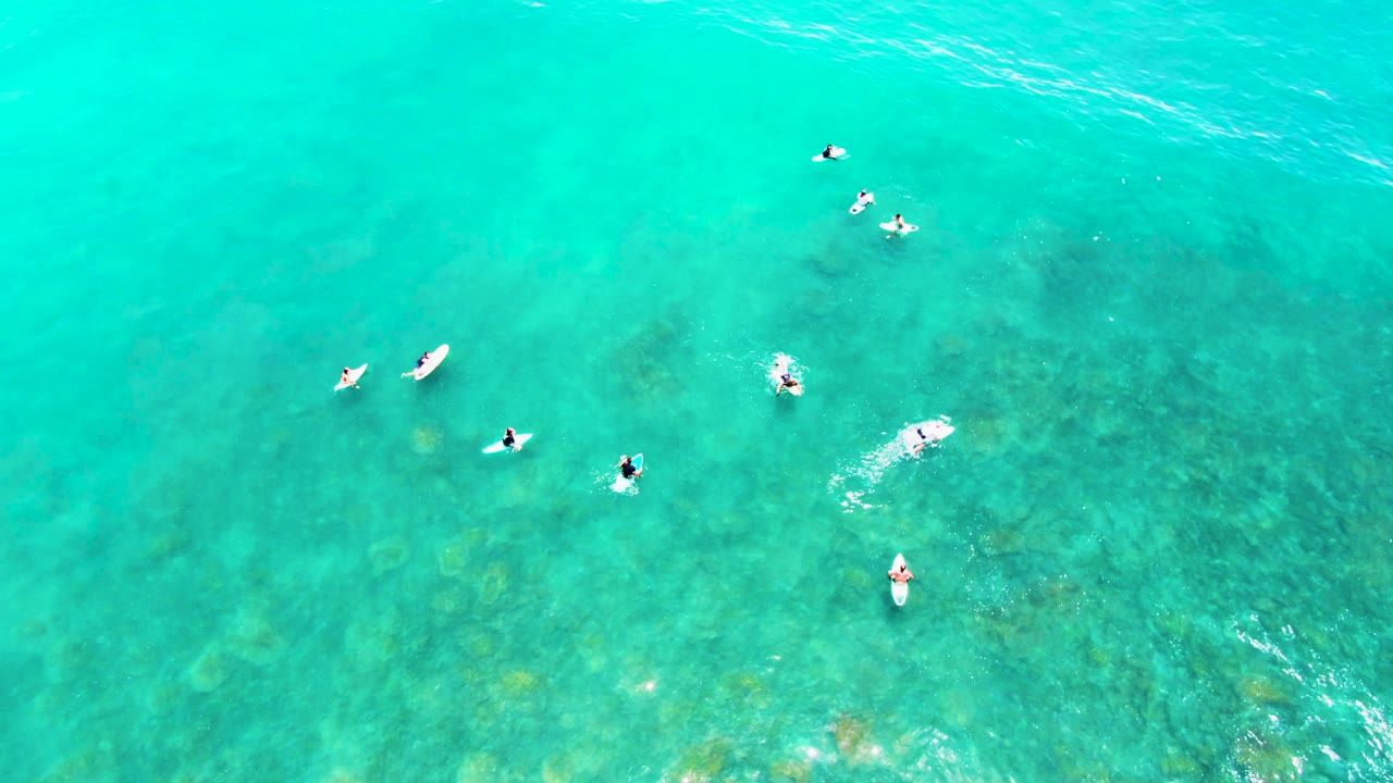 Swimmers and boards seen from above in clear blue-green water.