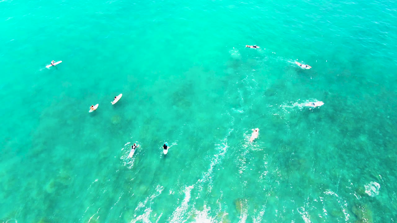 Overhead Punta Buzzards frame with swimmers and surfers spaced farther apart, white foam trails at midframe, and darker underwater areas visible through the water.