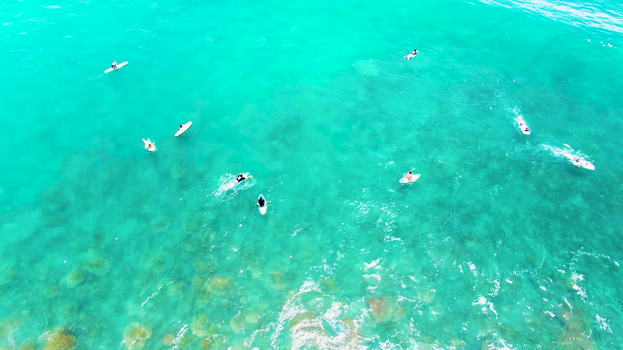 Surfers and surfboards scattered across bright turquoise water from above.