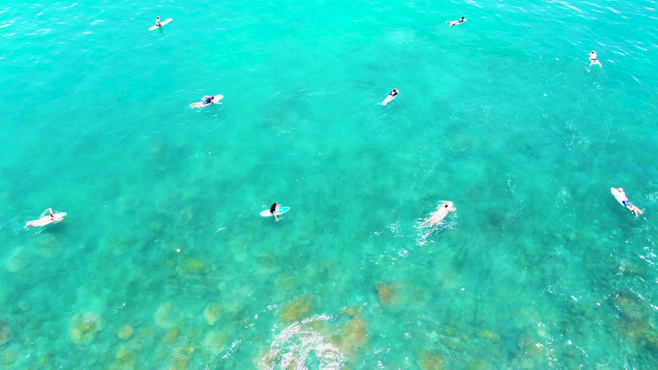 At 0:02, swimmers are visible across bright turquoise ocean at Punta Buzzards, with surface glints and muted seabed color beneath them.