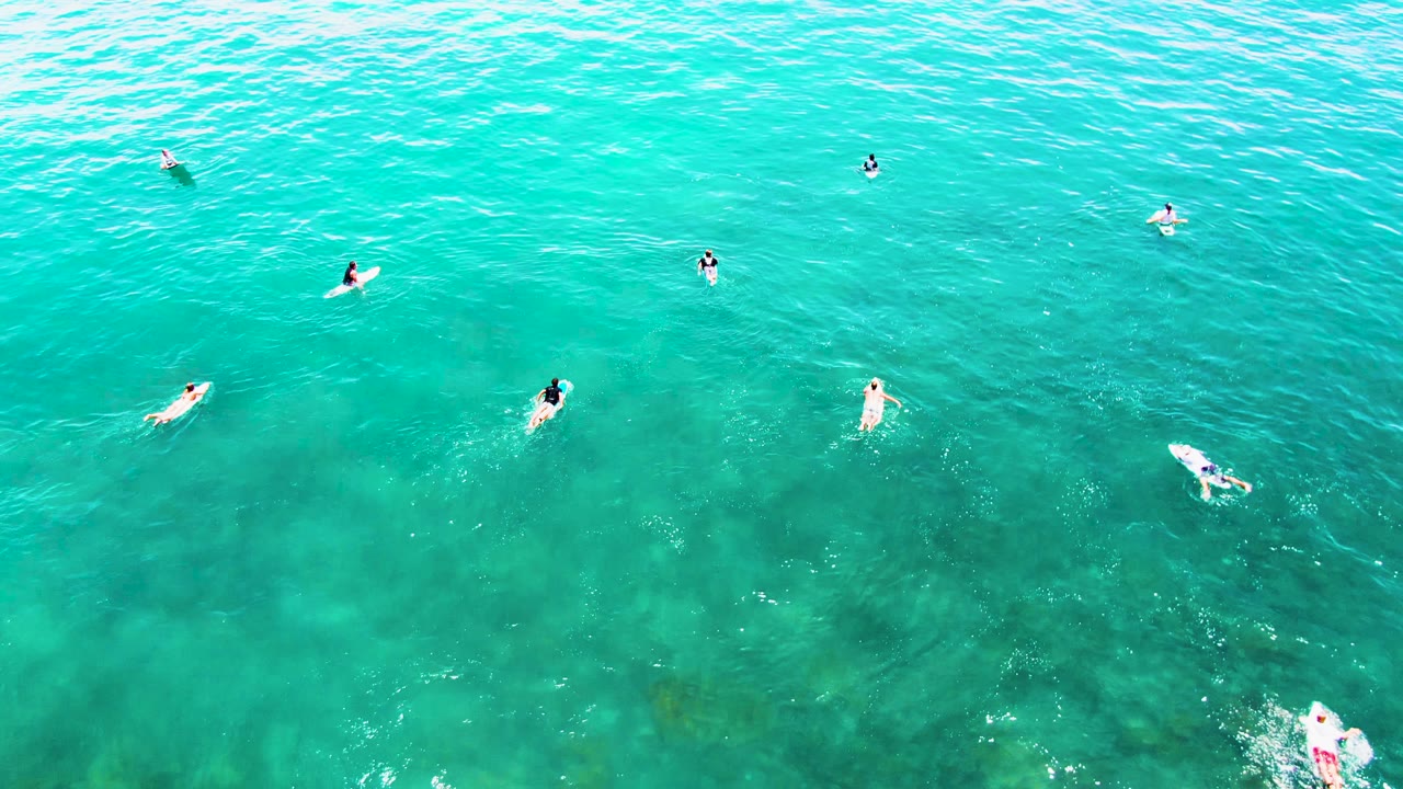 High overhead frame at Buzzards Beach showing people floating apart in green-blue water, with darker reef-like shapes visible beneath the surface.