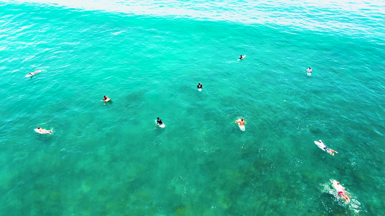 Swimmers and board riders floating below a broad wave line.
