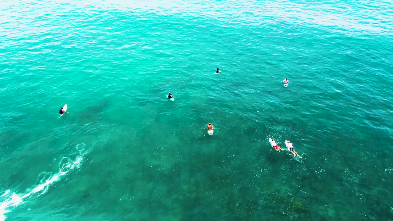 Overhead view of Punta Buzzards water with scattered distant surfers, two people close together on boards, and the earlier white wake thinning near the lower right.