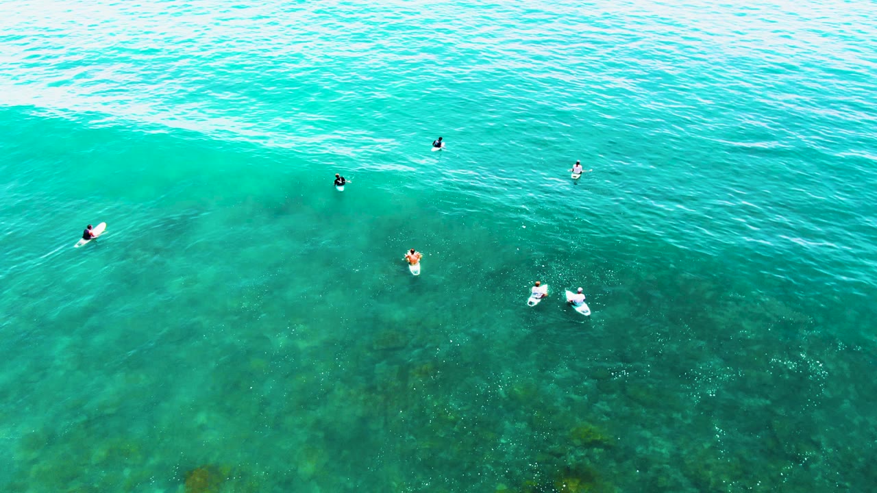 Surfers spaced across clear ocean with a wave band forming