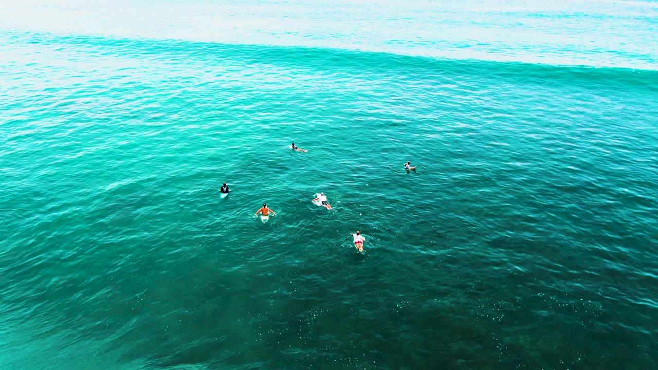 Small group of surfers float in clear water with swell behind them.