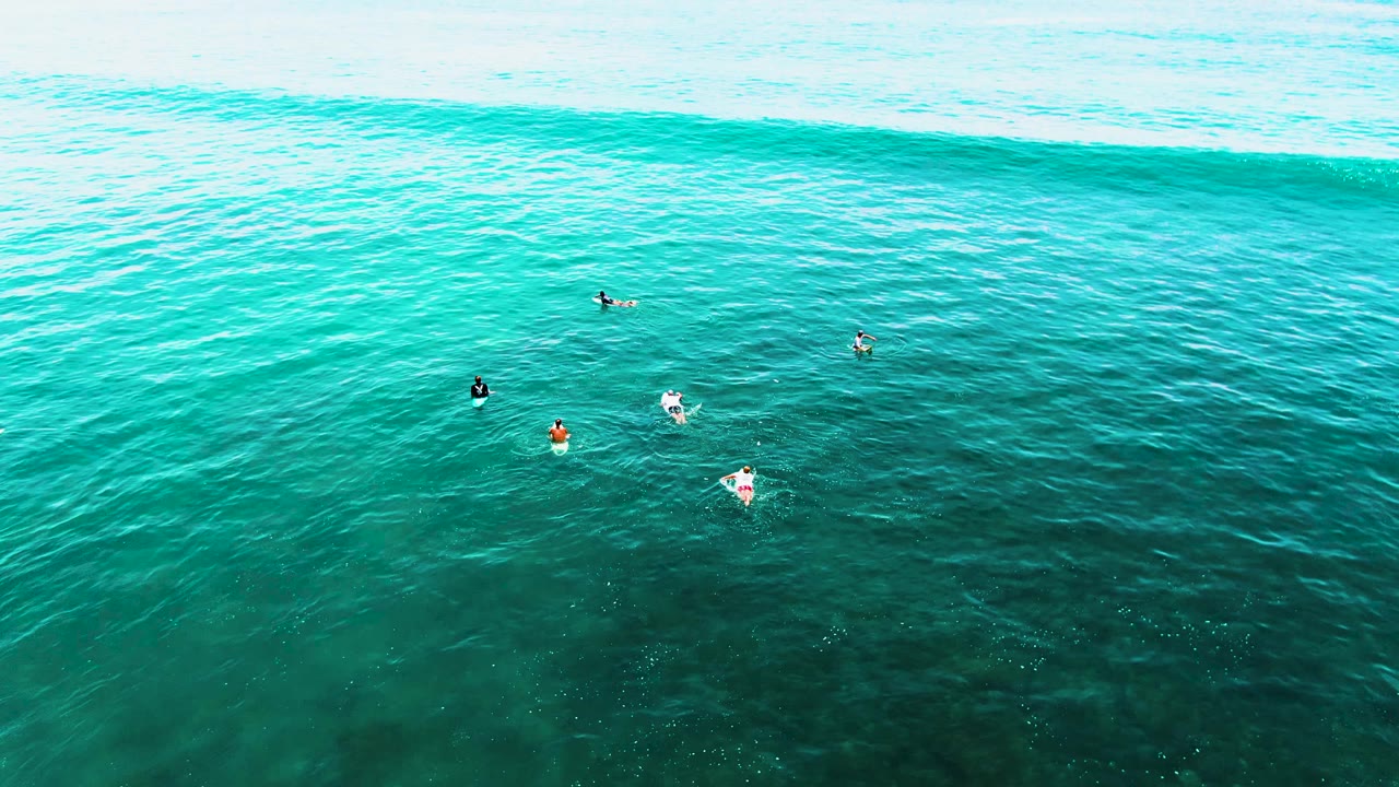 Overhead Punta Buzzards surf scene with multiple surfers visible as small figures, including bright boards against deep turquoise water and a wave band across the upper frame.