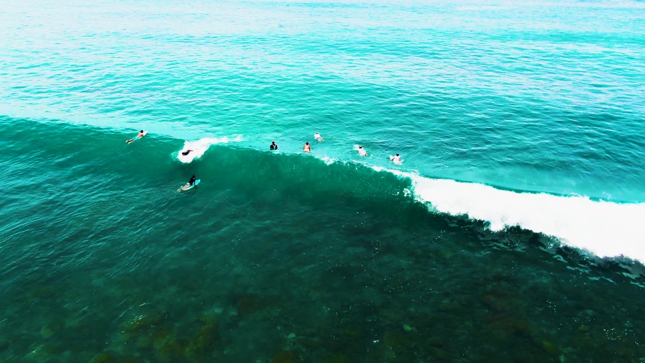 White foam breaks across the wave as surfers paddle nearby.