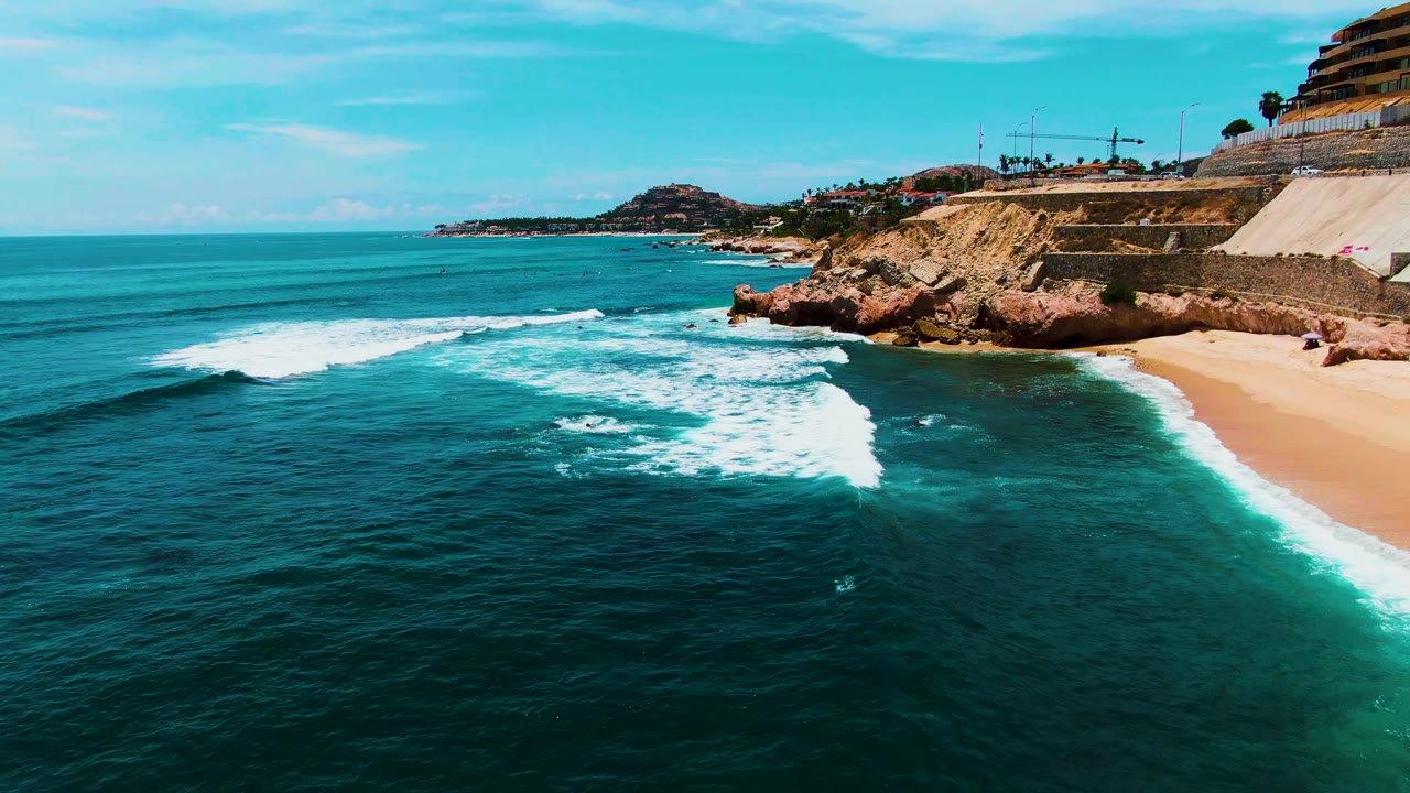 Foamy wave line rolls across dark blue water toward a beach.