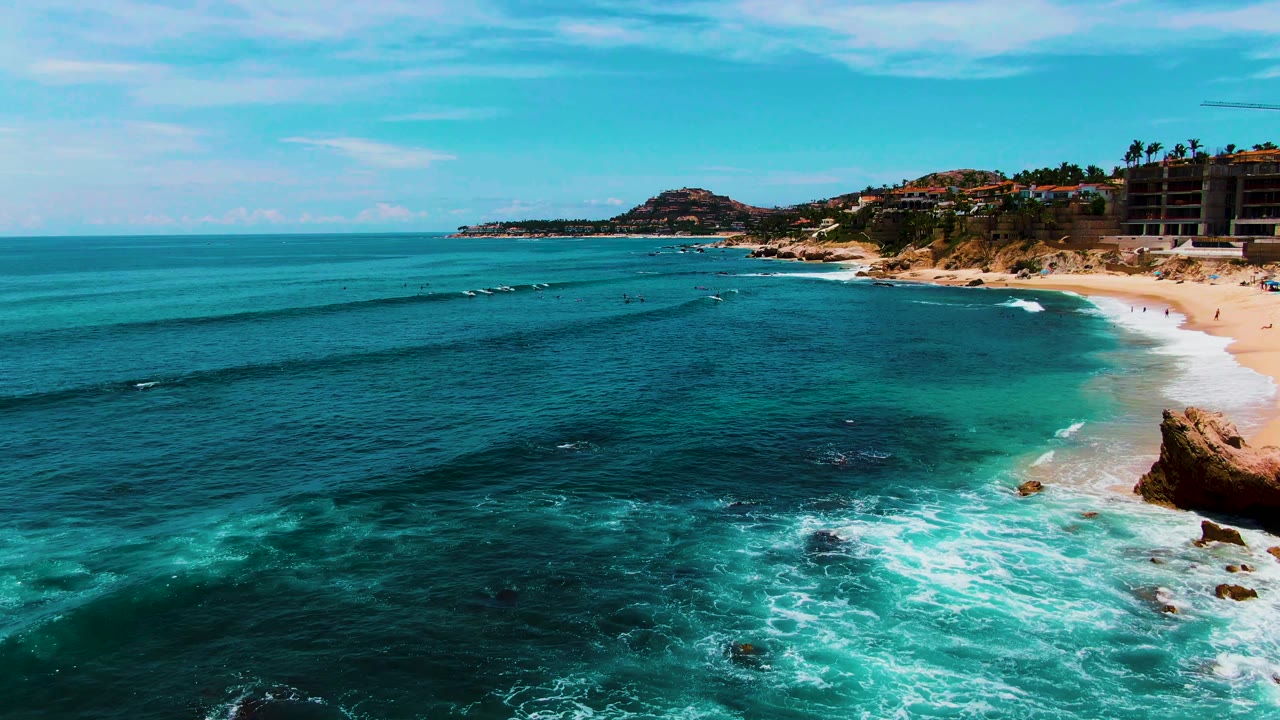 Wide aerial shoreline view with waves breaking toward a sandy beach.