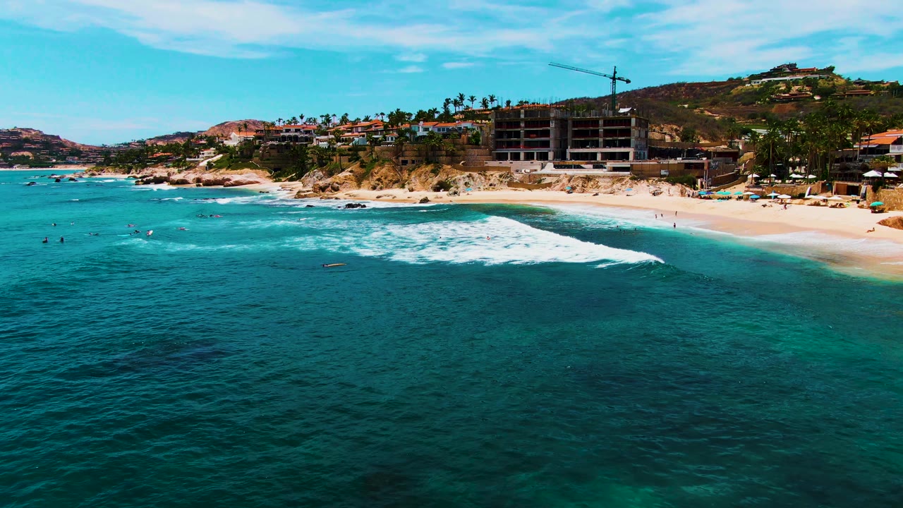 White surf breaks across shallow blue water beside a sandy beach.