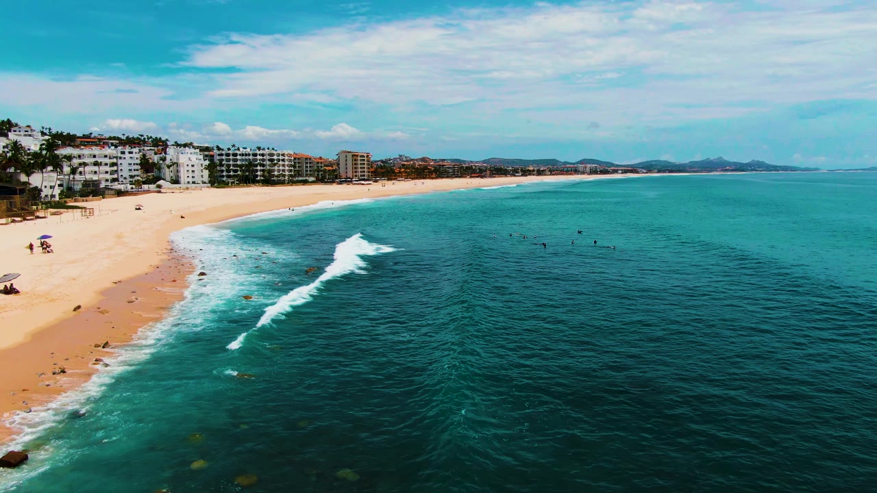 At 0:02, the breaking surf is more defined along the curved Buzzards Beach shoreline, with open turquoise water dominating the right side and no clearly visible people.