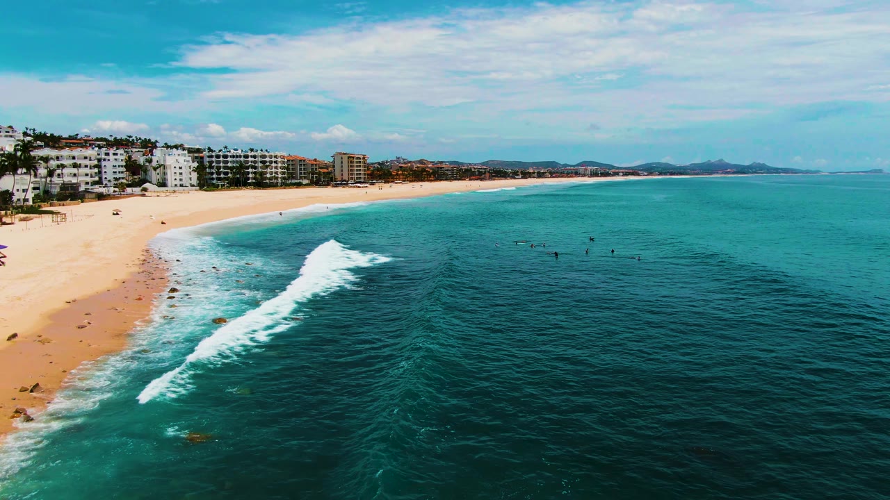 Larger white wave breaking beside sandy beach and ocean water