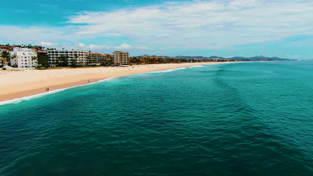 Aerial frame at Punta Buzzards, Baja California Sur showing the shoreline curving across the top, open turquoise water filling most of the frame, and a small remaining person or board near the lower edge.