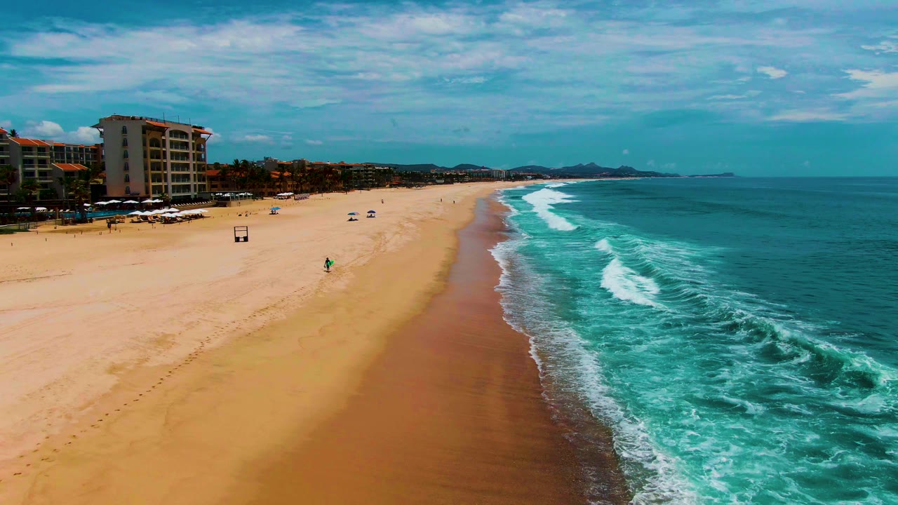 Wide beach shoreline with waves breaking and small people on the sand.