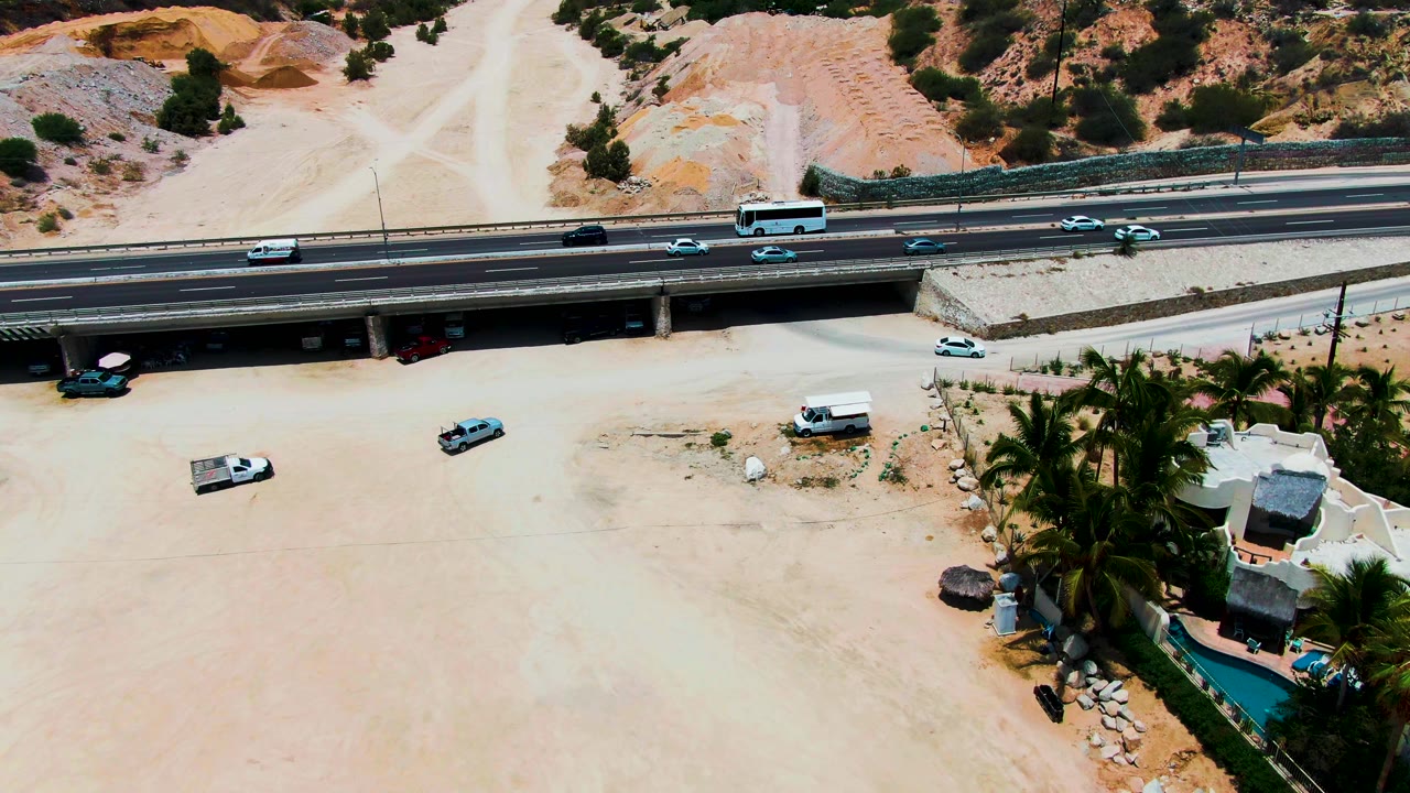 Aerial view of highway overpass above sandy ground and a palm-lined property.